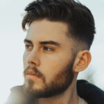 Vyras lauke su tamsiais plaukais ir taper fade kirpimu su tekstūruota viršutine dalimi