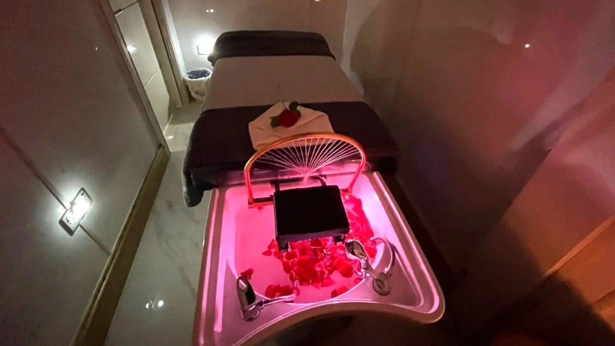 Jaukaus japoniško galvos SPA procedūrų kambario vidus su prislopinta šviesa: procedūrų gultas, dubuo su žiedlapiais ir SPA įranga