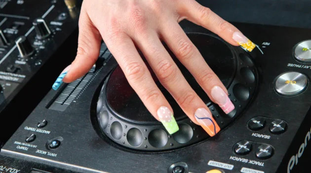 Ranka su electric mani, padėta ant Pioneer DJ grotuvo jog wheel, su neoniniais french tips gyvūnų ra&scaron;tu ir spiralėmis