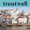 Baltai tinkuotas Algarve žvejų kaimelis su terakotinių stogų namais, kylančiais &scaron;laitu vir&scaron; ramaus vandens, mažos žvejų valtys, priri&scaron;tos palei krantinę, palmės ir bažnyčios bok&scaron;tas po giedru mėlynu dangumi.