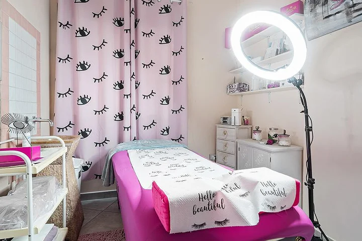 Rožinis procedūrų kambarys Centro Estetico Karma salone Olbia mieste su blakstienų raštu užuolaidomis, grožio lova ir apskritu šviestuvu.