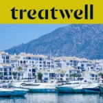 Puerto Banús prieplauka Marbella mieste, apsupta baltų daugiabučių ir prišvartuotų jachtų su kalnais fone, po geltona Treatwell vėliava.