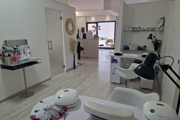 Priimamasis ir manikiūro zona Estetica Francesca salone Olbia mieste su apvaliu sieniniu veidrodžiu ir stiklinėmis lentynomis su grožio produktais.