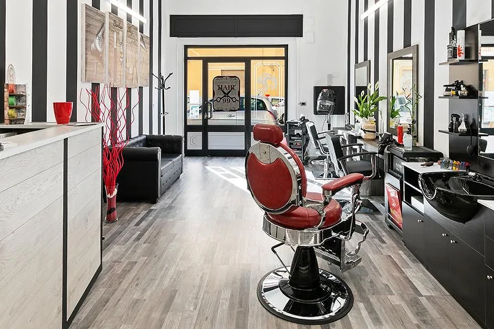 Raudona vintažinė barzdaskučio kėdė Hair 99 salone Alghero su būdingomis juodai baltomis juostuotomis sienomis.